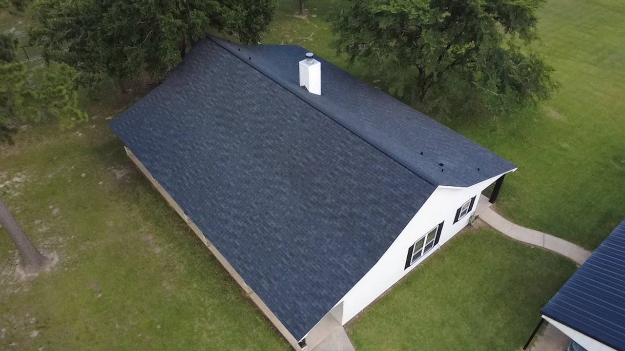 Aerial view of a white home with a new dark shingle roof