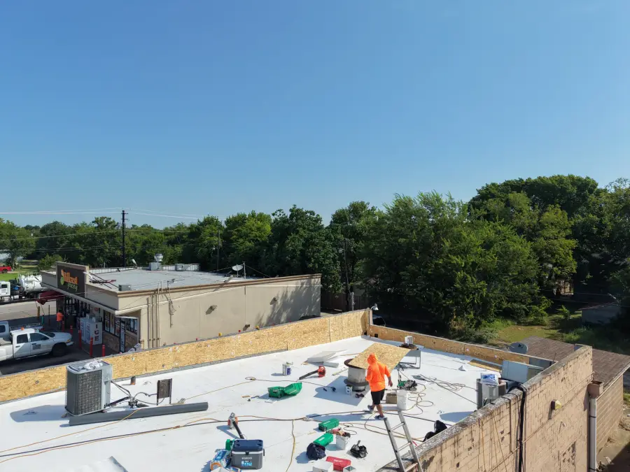Crew installing a white flat roof membrane on a commercial building