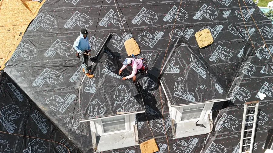 Crew members installing roof underlayment on a steep home