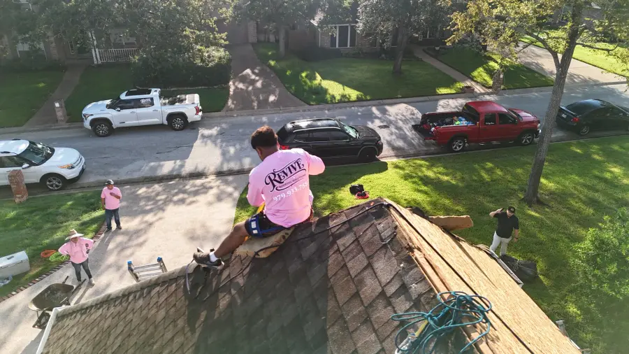 Crew member installing shingles on a home while the team works below