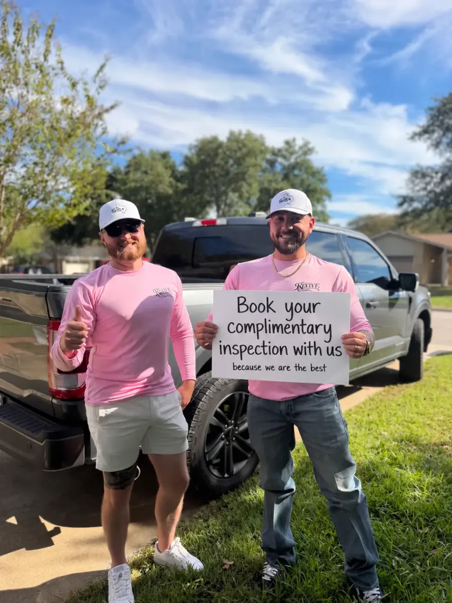 Two Revive Roofing Solutions team members holding a sign that reads book your complimentary inspection
