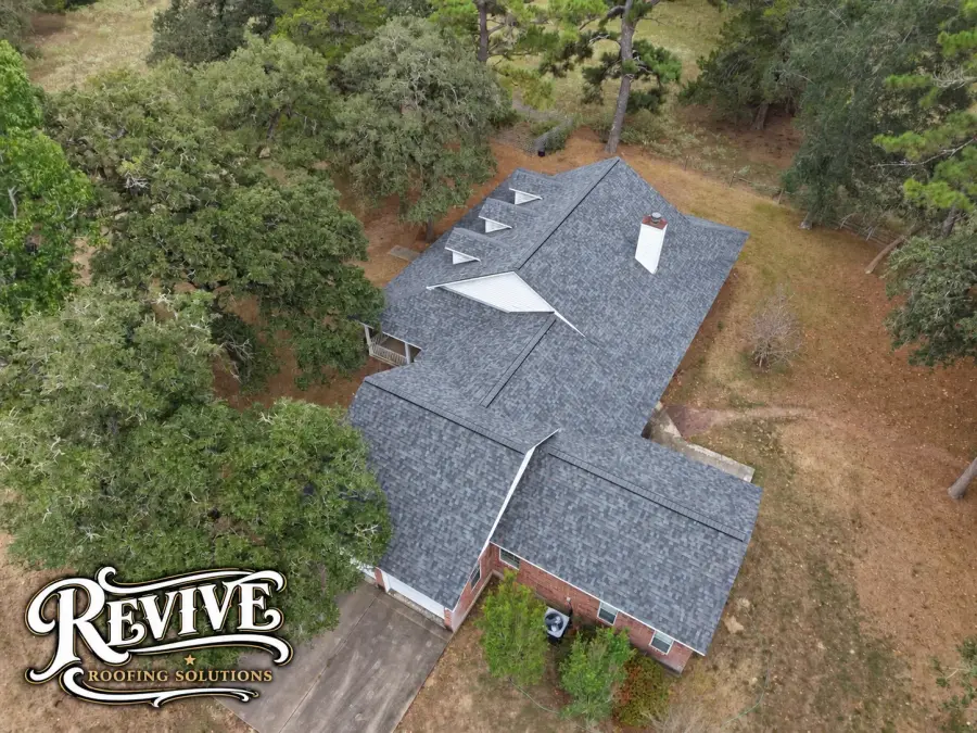 Aerial view of a wooded property with a new gray shingle roof