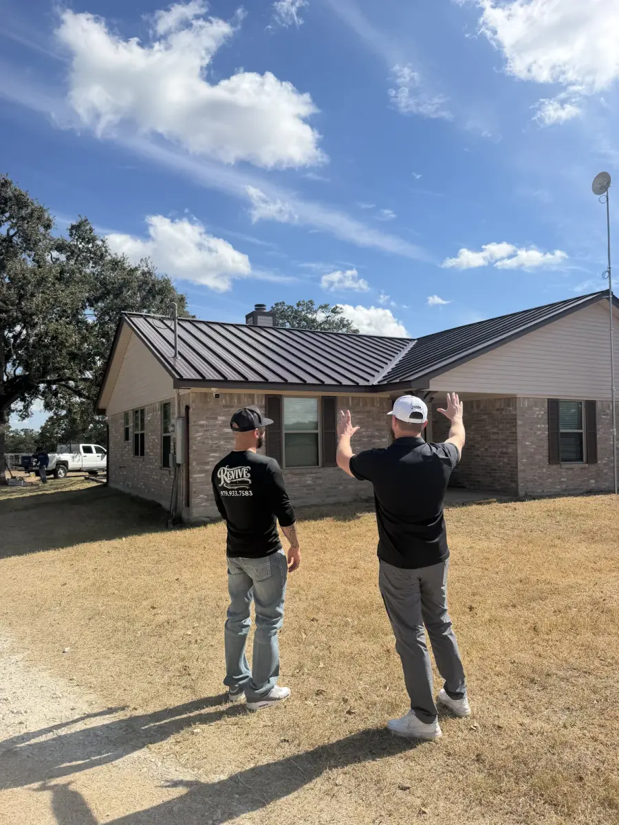 Two Revive team members in front of a brick home with a dark standing seam metal roof