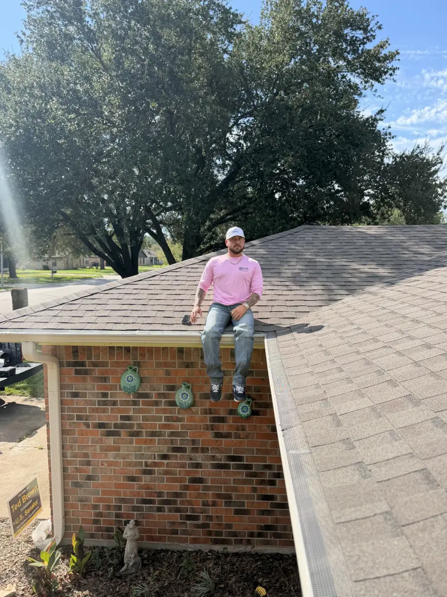 Revive team member sitting on the edge of a new shingle roof on a brick home