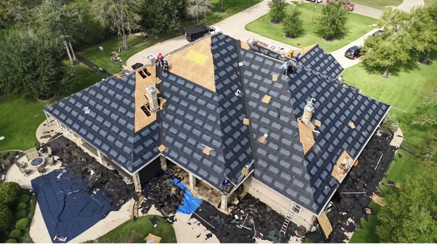 Aerial view of a shingle roof replacement in progress on a large home