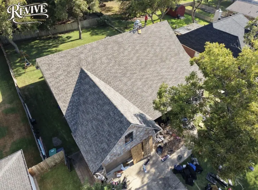 Aerial view of a gray shingle roof on a home with mature trees, with the Revive logo